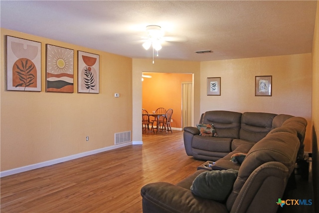 living room featuring wood-type flooring, ceiling fan, and a textured ceiling