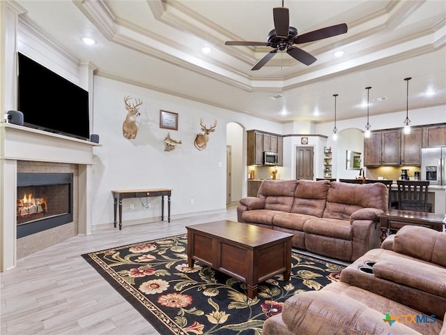 living room with light hardwood / wood-style flooring, ceiling fan, a fireplace, and a raised ceiling