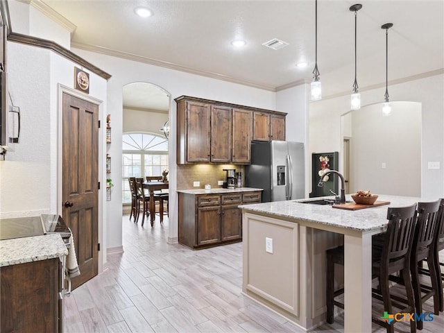 kitchen featuring hanging light fixtures, light stone countertops, an island with sink, and stainless steel appliances