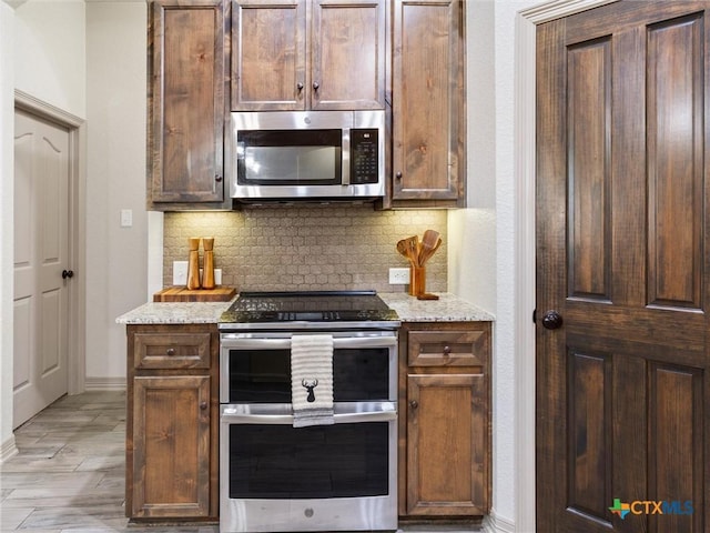 kitchen with light stone countertops, backsplash, appliances with stainless steel finishes, and dark brown cabinetry