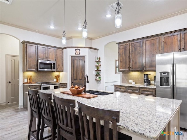 kitchen featuring pendant lighting, stainless steel appliances, an island with sink, sink, and light stone counters