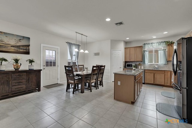 kitchen with black refrigerator with ice dispenser, stainless steel microwave, a kitchen island, healthy amount of natural light, and recessed lighting