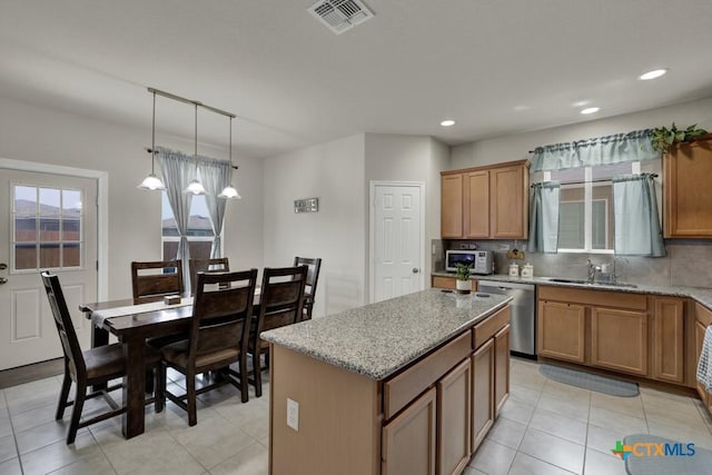 kitchen featuring dishwasher, a sink, a kitchen island, light stone countertops, and brown cabinets