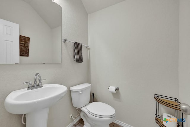 half bath with a sink, lofted ceiling, toilet, and baseboards