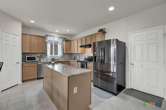 kitchen featuring stainless steel appliances, under cabinet range hood, a kitchen island, light stone counters, and decorative backsplash