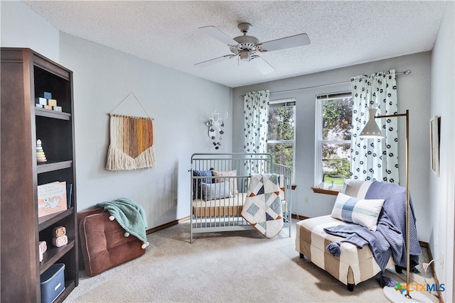 carpeted bedroom with a textured ceiling, a nursery area, and ceiling fan