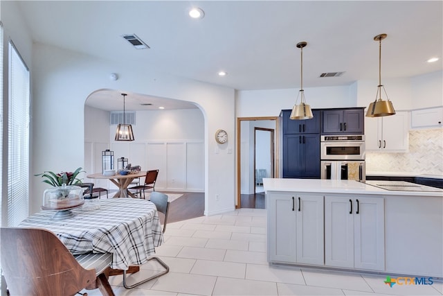 kitchen with backsplash, pendant lighting, white cabinets, double oven, and light hardwood / wood-style flooring