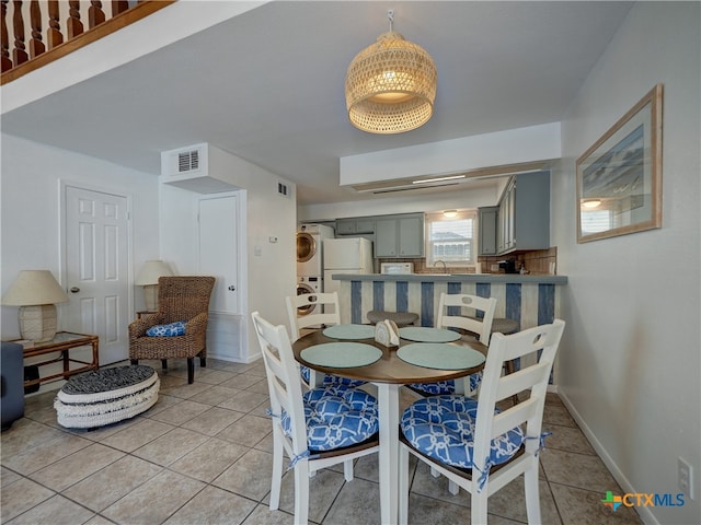 tiled dining room with stacked washer and clothes dryer and sink