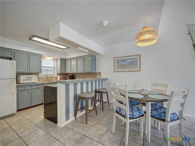 kitchen featuring kitchen peninsula, a breakfast bar area, light tile patterned floors, hanging light fixtures, and white appliances