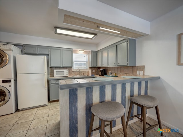 kitchen featuring stacked washer / dryer, tasteful backsplash, white appliances, a kitchen bar, and kitchen peninsula