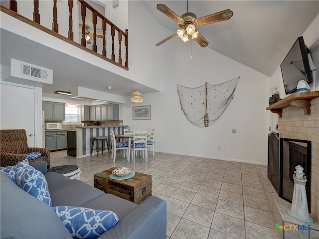 tiled living room with a brick fireplace, ceiling fan, sink, and high vaulted ceiling