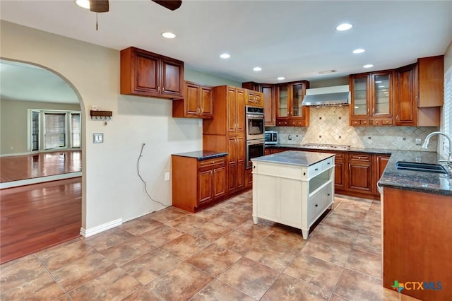 608 Chimney Rock Dr, Victoria, TX 77904 - kitchen featuring a sink, ceiling fan, arched walkways, wall chimney range hood, and appliances with stainless steel finishes