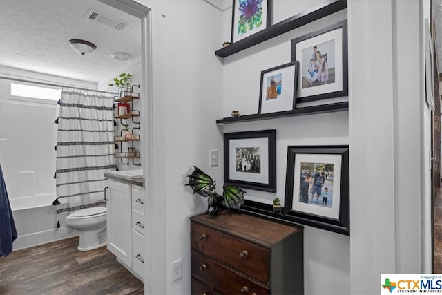 full bathroom featuring hardwood / wood-style flooring, a textured ceiling, shower / bathtub combination with curtain, vanity, and toilet