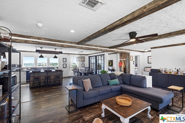 living room featuring dark wood-type flooring, beamed ceiling, ceiling fan, and a textured ceiling