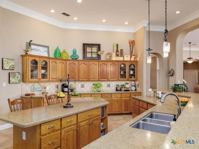 kitchen with hanging light fixtures, sink, ornamental molding, light tile patterned flooring, and a breakfast bar