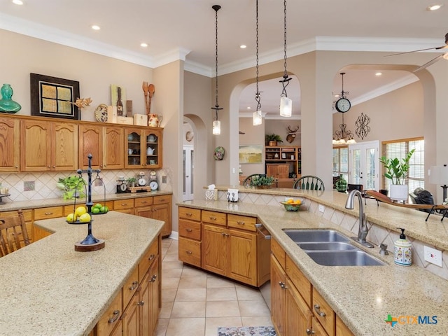 kitchen with light stone counters, ornamental molding, light tile patterned flooring, hanging light fixtures, and sink