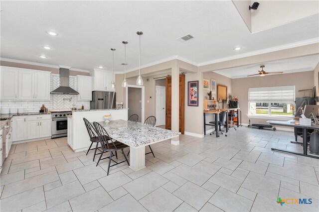 kitchen featuring a kitchen bar, appliances with stainless steel finishes, wall chimney exhaust hood, pendant lighting, and white cabinetry