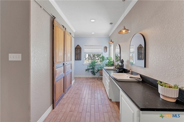 kitchen with crown molding, hanging light fixtures, light hardwood / wood-style flooring, a barn door, and white cabinetry