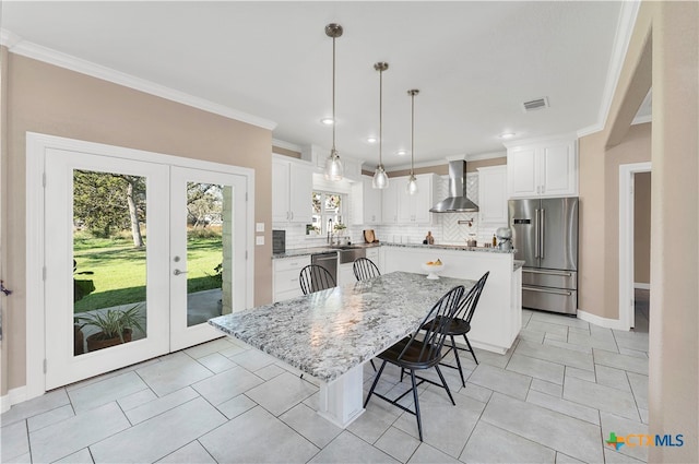 kitchen featuring white cabinetry, a kitchen island, wall chimney range hood, and appliances with stainless steel finishes