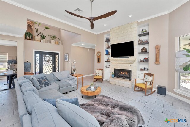 tiled living room with a fireplace, built in shelves, ceiling fan, and ornamental molding