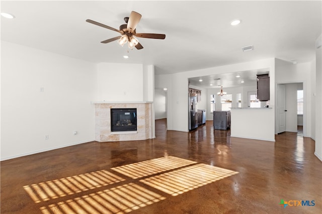 unfurnished living room with ceiling fan with notable chandelier and a tile fireplace