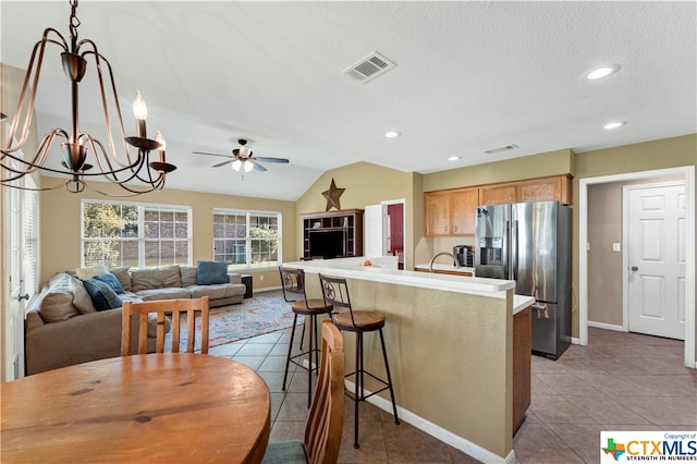 kitchen with stainless steel fridge, a breakfast bar, a center island with sink, lofted ceiling, and light tile patterned flooring