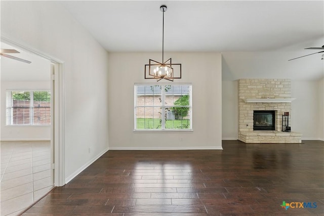 unfurnished living room with dark wood finished floors, a brick fireplace, baseboards, and ceiling fan with notable chandelier