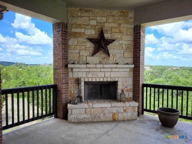 view of patio / terrace with an outdoor stone fireplace, a balcony, and a wooded view