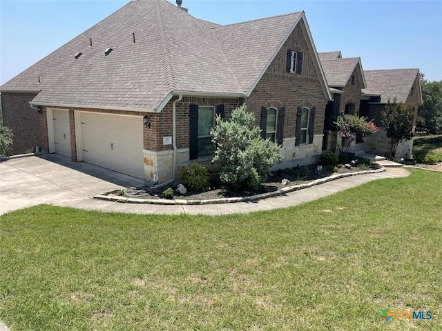 view of front of house with a front yard, driveway, an attached garage, a shingled roof, and brick siding