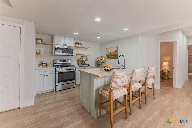 kitchen with open shelves, wooden counters, appliances with stainless steel finishes, a sink, and a kitchen breakfast bar