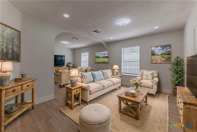 living room featuring arched walkways, recessed lighting, visible vents, wood finished floors, and baseboards