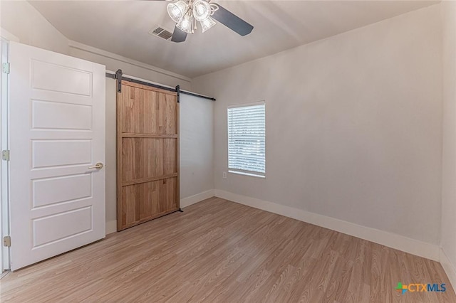 unfurnished bedroom with visible vents, light wood-style flooring, a barn door, ceiling fan, and baseboards