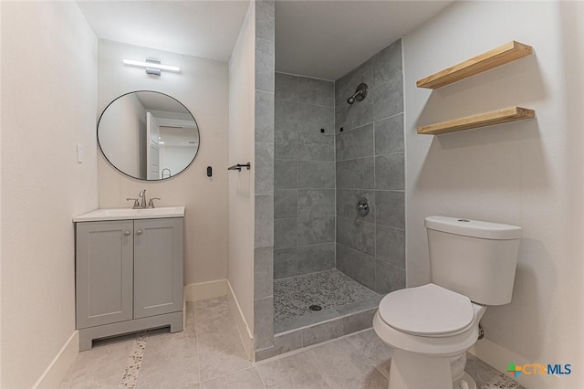 full bath featuring toilet, baseboards, tiled shower, and vanity