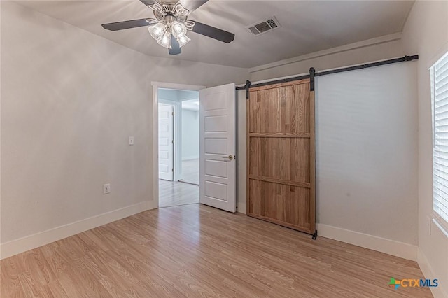 unfurnished bedroom featuring ceiling fan, a barn door, visible vents, baseboards, and light wood-style floors