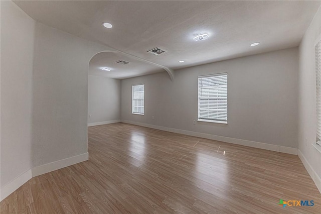 empty room with baseboards, visible vents, arched walkways, wood finished floors, and recessed lighting