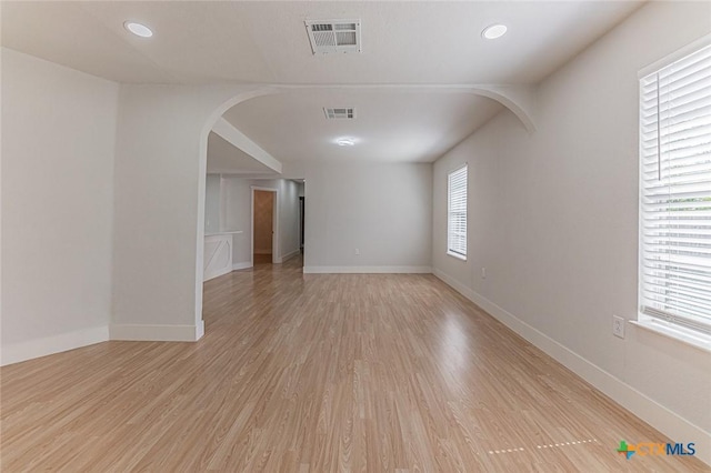 spare room featuring arched walkways, light wood-type flooring, visible vents, and baseboards