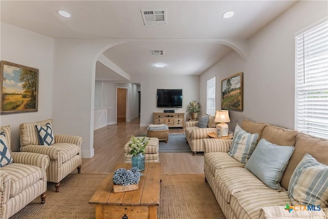 living room with light wood-style floors, arched walkways, a healthy amount of sunlight, and visible vents