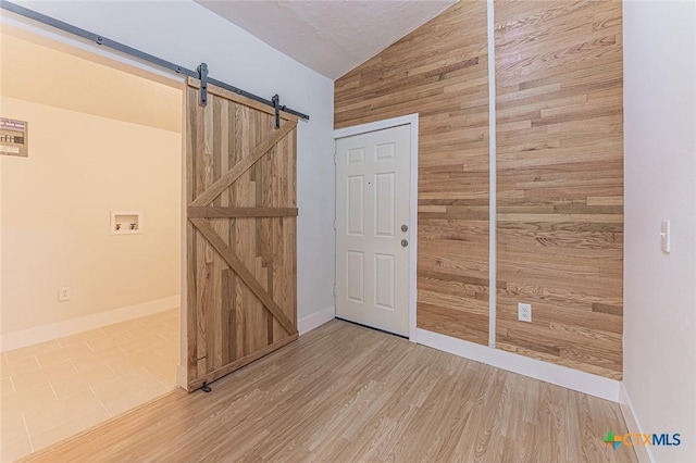 unfurnished room with lofted ceiling, wood walls, light wood finished floors, and a barn door