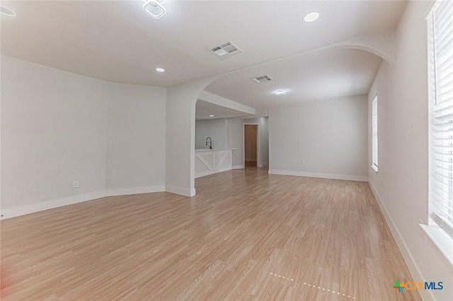 unfurnished room with light wood-type flooring, visible vents, arched walkways, and baseboards