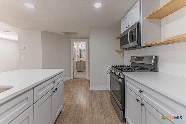 kitchen featuring appliances with stainless steel finishes, light countertops, light wood finished floors, and open shelves