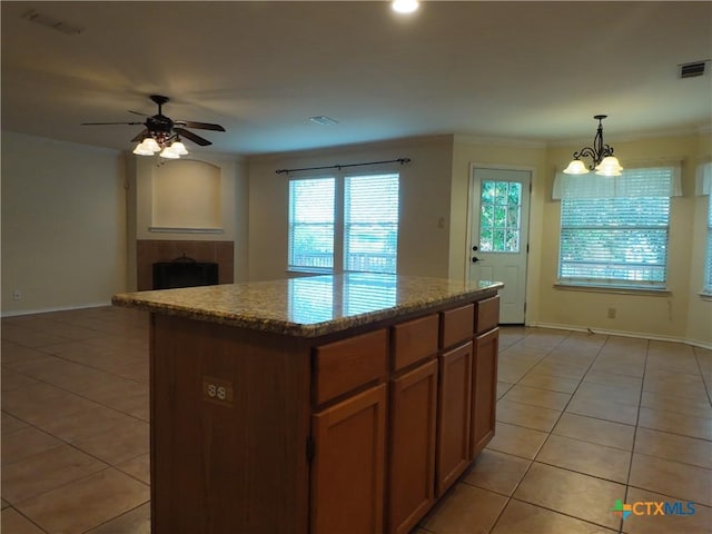 kitchen with pendant lighting, a center island, ceiling fan with notable chandelier, light tile patterned floors, and a fireplace