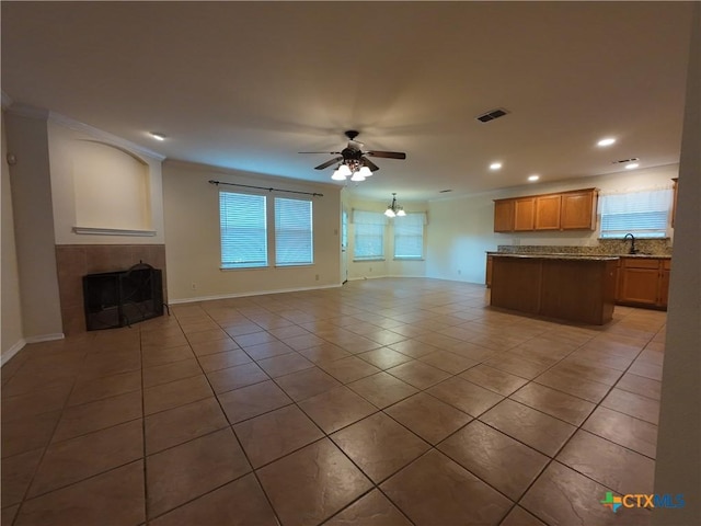 unfurnished living room featuring sink, a fireplace, light tile patterned floors, ceiling fan with notable chandelier, and ornamental molding