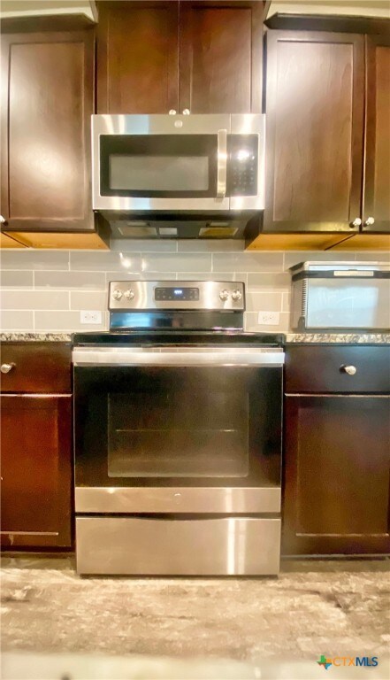 kitchen featuring backsplash, appliances with stainless steel finishes, dark brown cabinetry, and light stone countertops