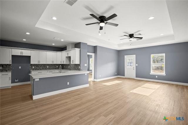 kitchen featuring a raised ceiling, ceiling fan, tasteful backsplash, light hardwood / wood-style floors, and white cabinetry