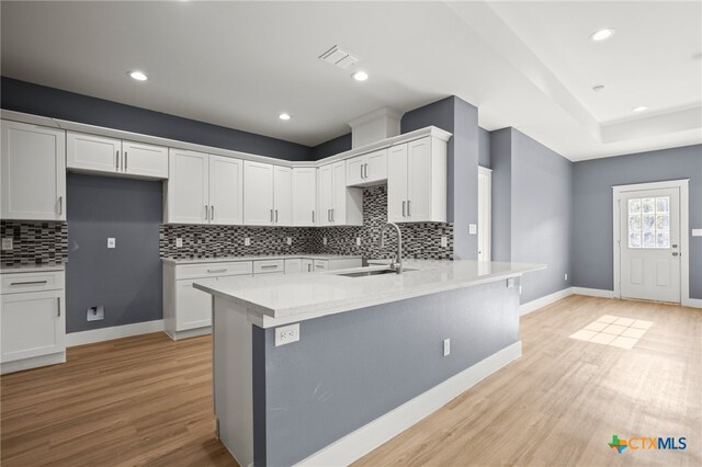 kitchen with decorative backsplash, light wood-type flooring, white cabinetry, and sink