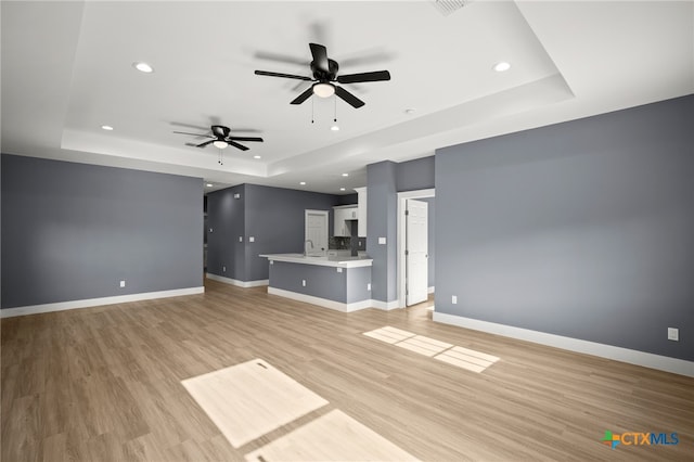 unfurnished living room with ceiling fan, a raised ceiling, light wood-type flooring, and sink