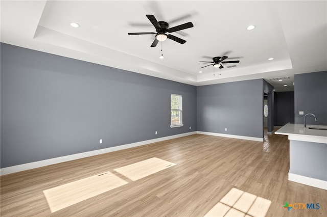 unfurnished living room featuring a tray ceiling, ceiling fan, sink, and light hardwood / wood-style floors