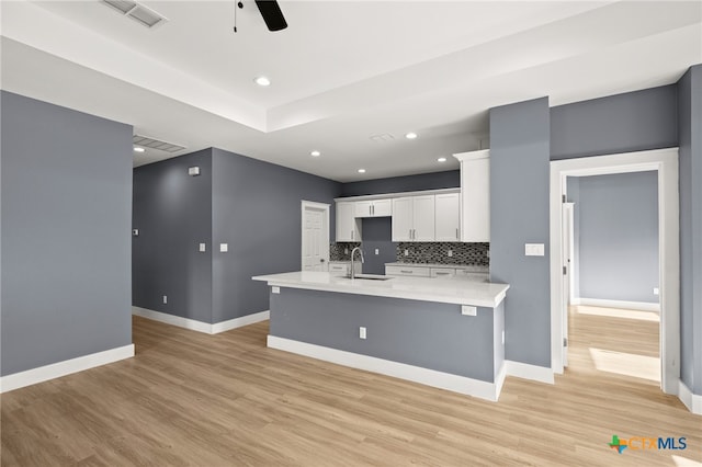 kitchen with white cabinets, backsplash, light hardwood / wood-style floors, and sink