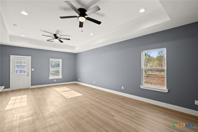 spare room with a tray ceiling, a wealth of natural light, ceiling fan, and light wood-type flooring