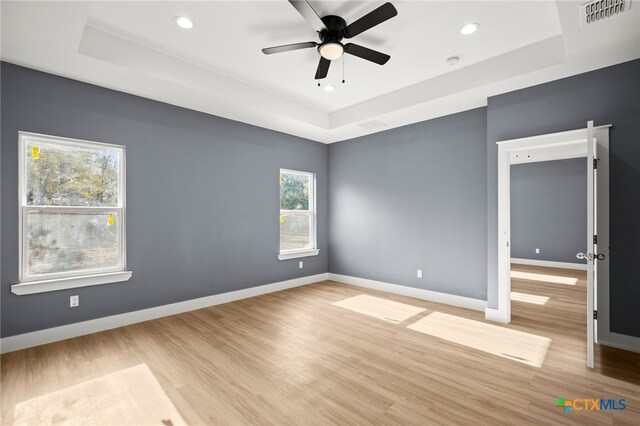 spare room featuring a tray ceiling, ceiling fan, and light hardwood / wood-style flooring